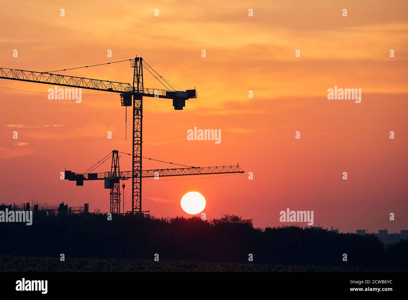 Activité de construction sur le site de construction. Silhouettes de grues contre le soleil. Banque D'Images