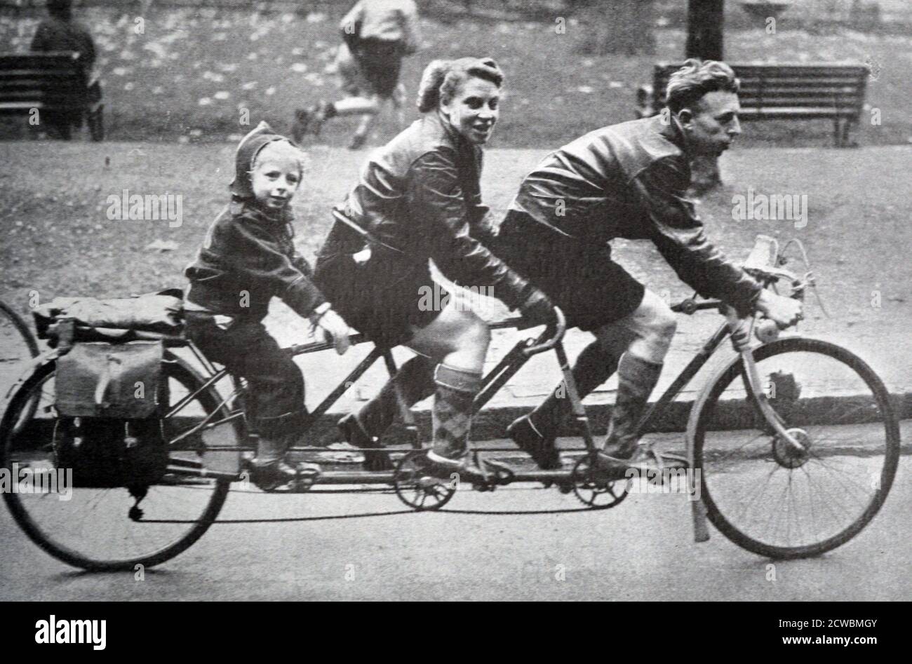 Photographie en noir et blanc d'une famille qui fait du vélo pour trois personnes, dont un père, sa jeune femme et son enfant. Banque D'Images