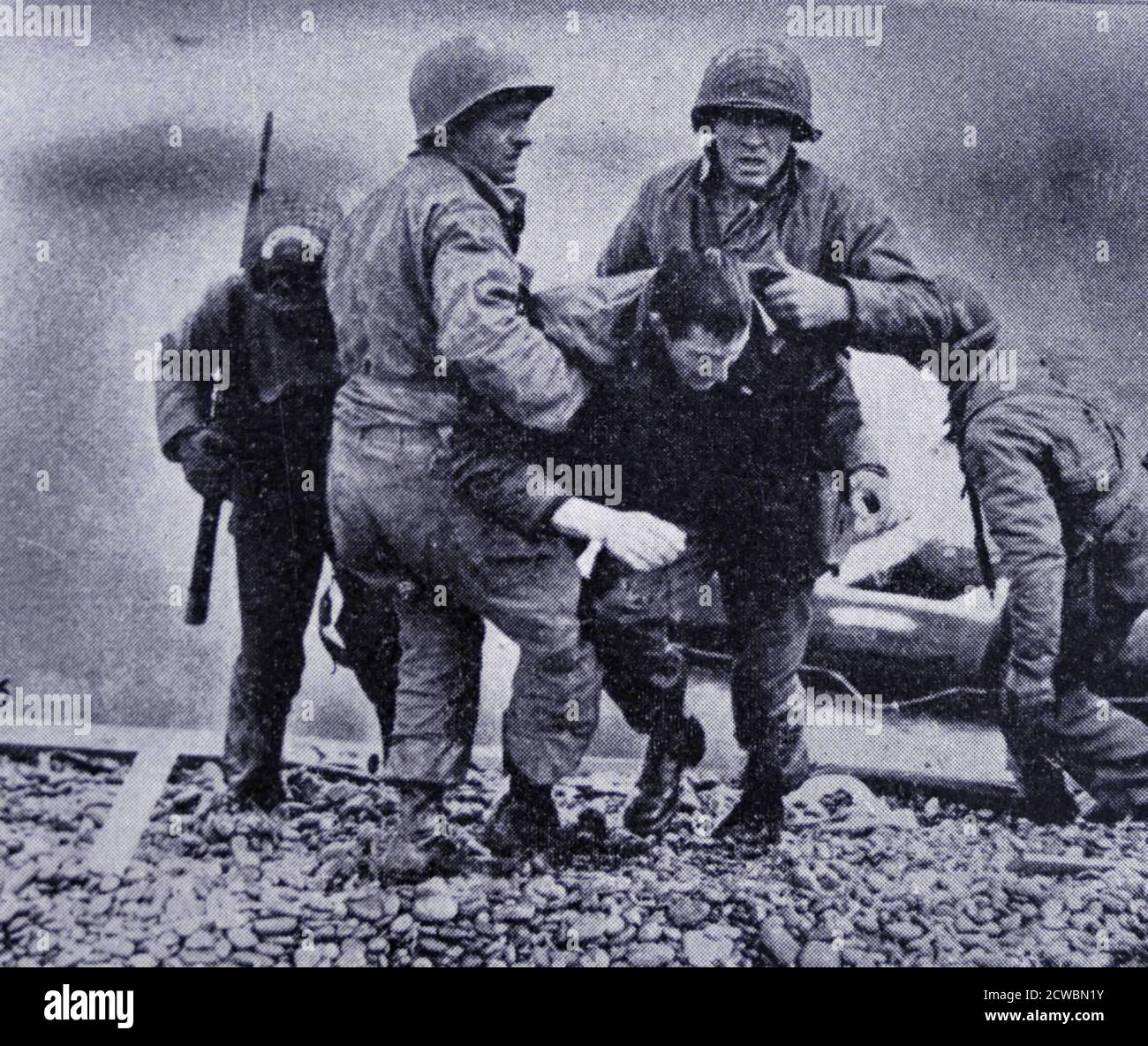Photographie en noir et blanc de la Seconde Guerre mondiale (1939-1945) montrant des images de l'invasion de la mer par les alliés en Normandie le jour J, 6 juin 1944; les soldats américains aident un de leurs camarades qui a été blessé à l'avance sur la plage. Banque D'Images