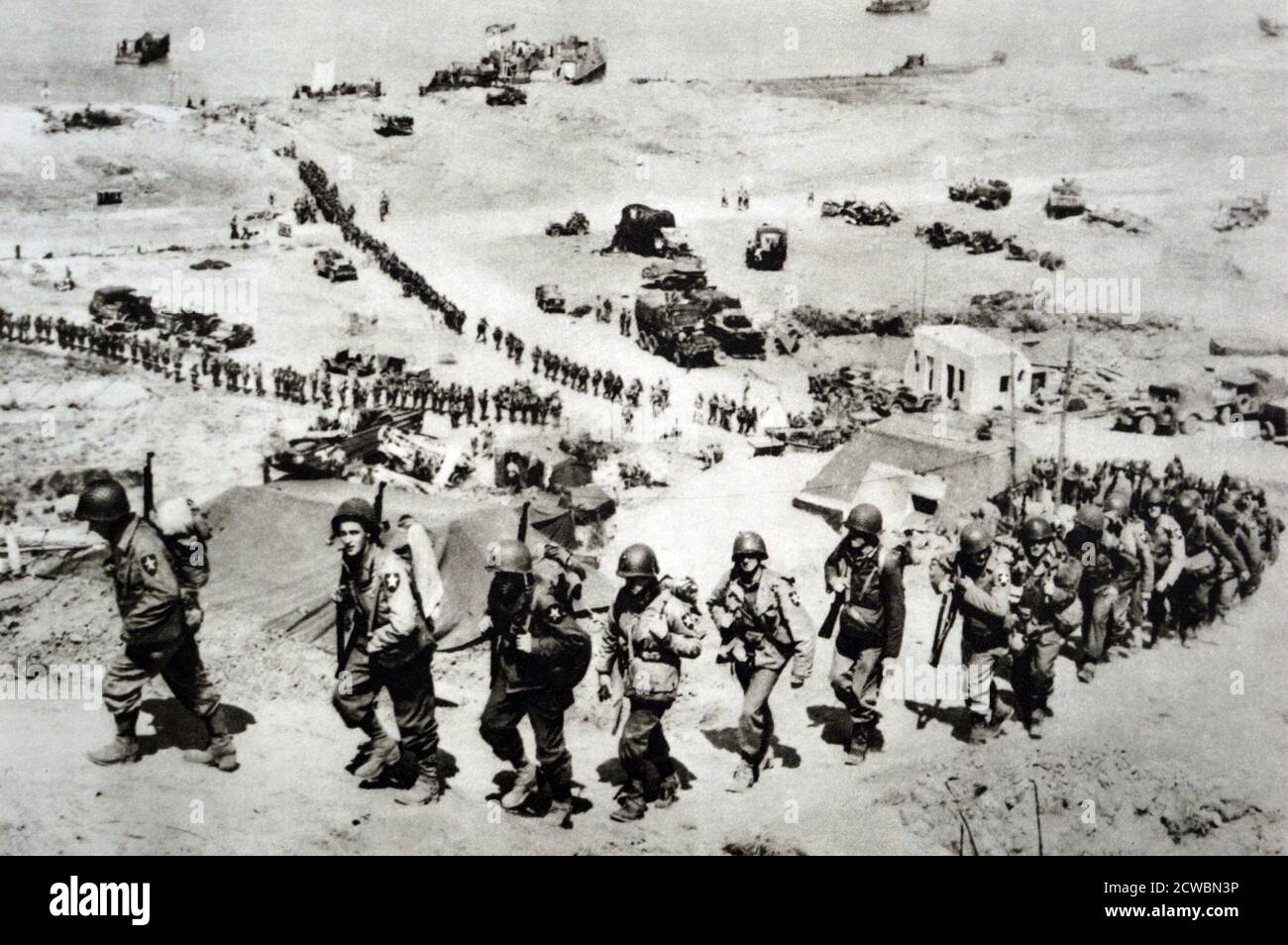 Photographie en noir et blanc de la Seconde Guerre mondiale (1939-1945) montrant les troupes américaines débarquant en Normandie le 6 juin 1944 ; vue depuis le sommet d'une colline surplombant la mer et les troupes américaines marchant sur la colline. Banque D'Images
