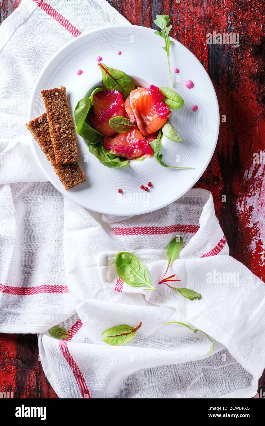 Assiette en céramique blanche avec filet de saumon coupé en tranches, salé avec du jus de betterave, servi avec des toasts de blé entier, des feuilles de salade et de la sauce aux betteraves sur du chou rouge Banque D'Images