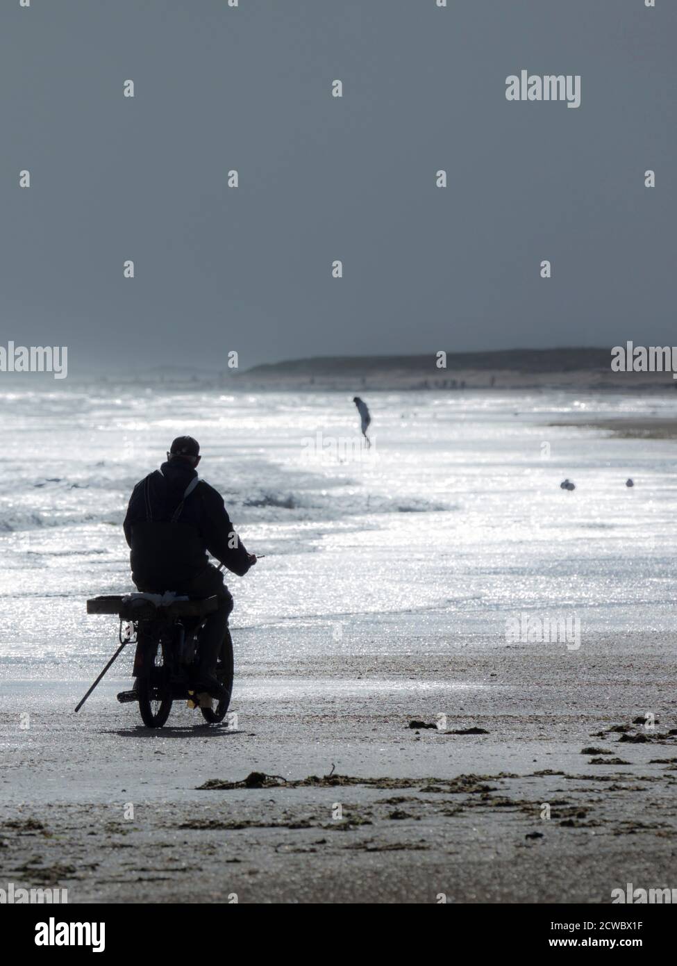 Homme plus âgé sur un cyclomoteur le long d'une plage journée brumeuse Banque D'Images