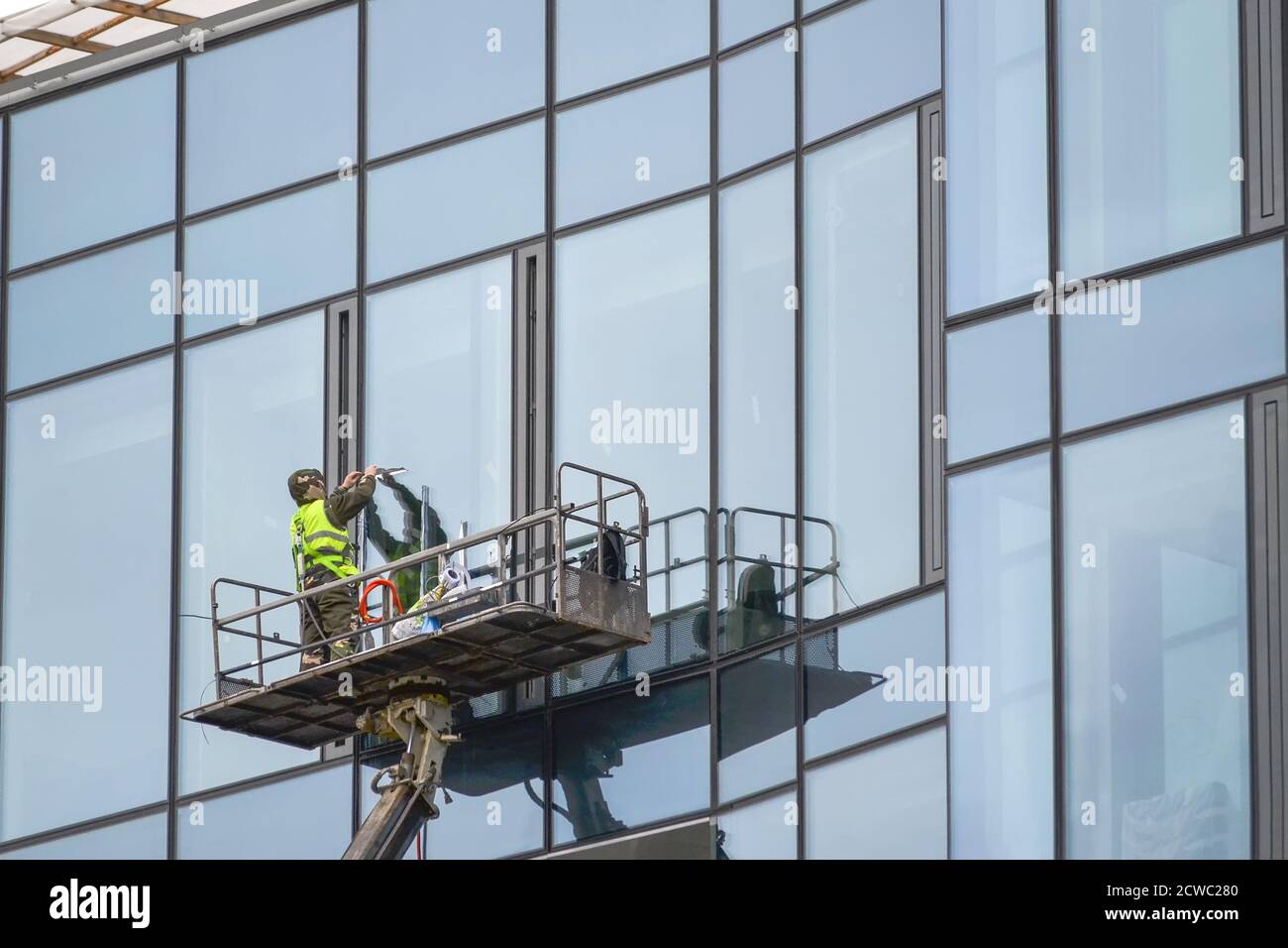 Un travailleur en combinaison sur un ascenseur lave la paroi en verre d'un bâtiment. Banque D'Images