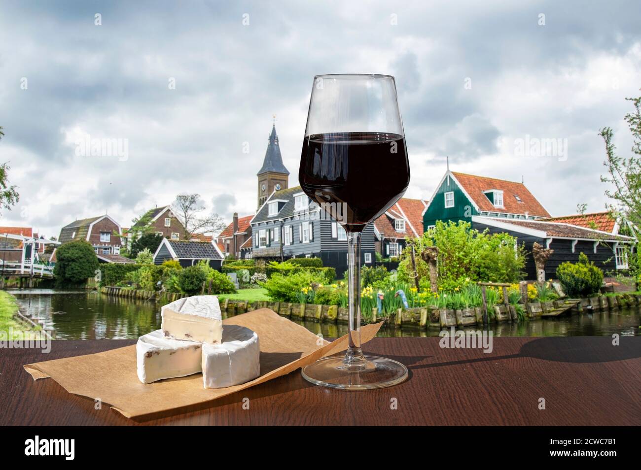 Verre de vin rouge et chhese de brie avec vue sur le canal, le pont et les maisons de pêche traditionnelles en bois dans le village de Marken, pays-Bas. Banque D'Images