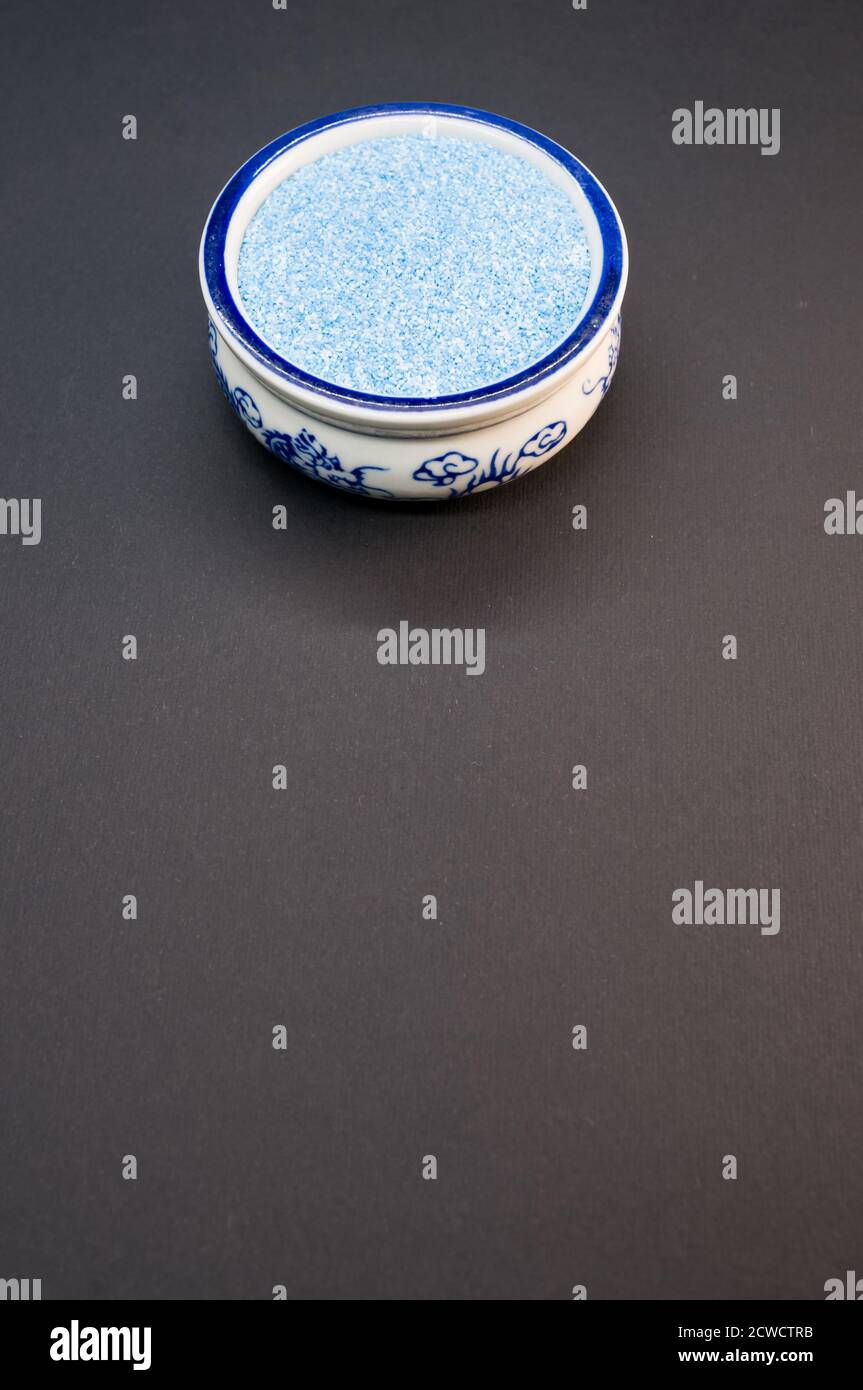 Plan vertical de sable bleu dans un bol de chine sur une surface noire Banque D'Images