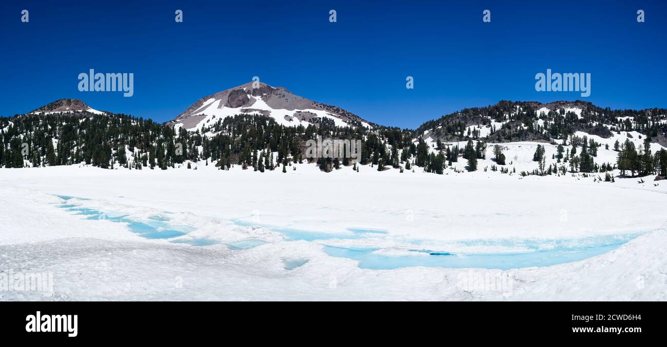Forêt et montagne à l'arrière du lac Helen, couverte de glace et de neige en juillet, par une journée ensoleillée avec un ciel bleu de montagne. Parc national de Lassen. Banque D'Images