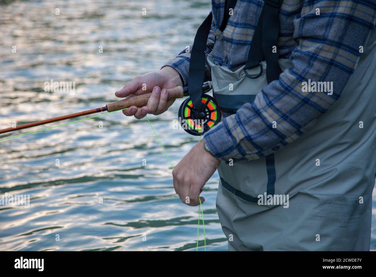 Un gros plan d'un pêcheur de mouche portant une chemise à carreaux, tenant une tige et un rabatteur tout en barbotant dans l'eau à Vancouver, en Colombie-Britannique Banque D'Images