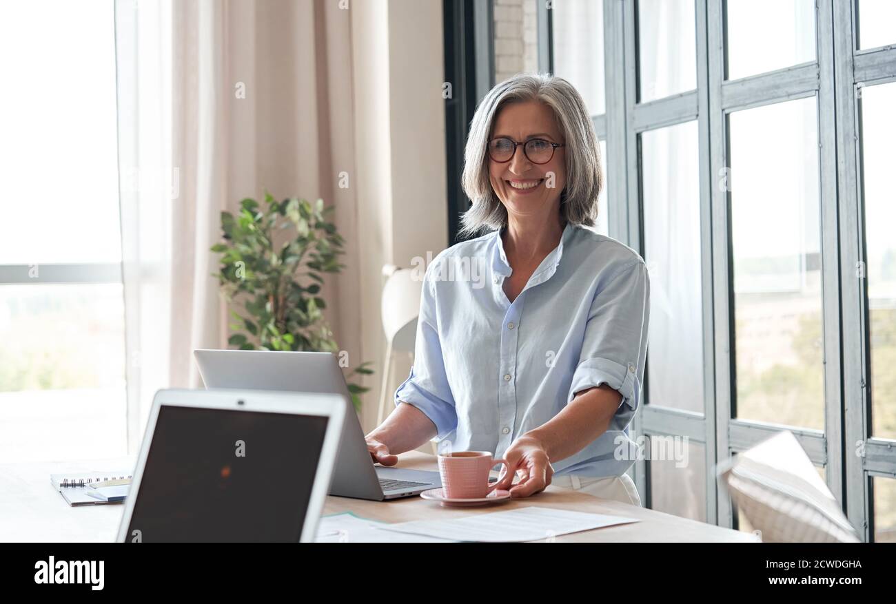 Bonne vieille femme mentor, coach ou enseignante debout à table pendant l'atelier. Banque D'Images