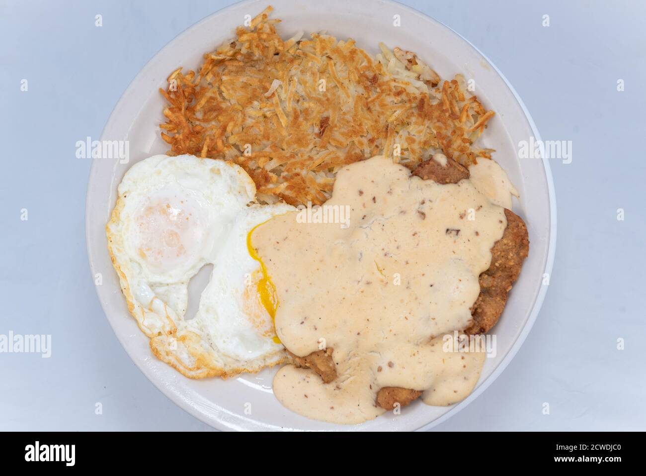 Vue en hauteur d'un copieux repas composé d'un steak de poulet frit, d'œufs et de pommes de terre sautées avec de la sauce campagnarde. Banque D'Images