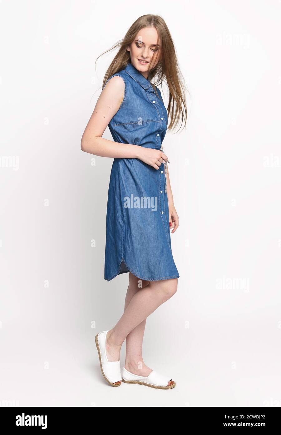 Belle jeune femme gaie dans une robe en denim bleu sur fond blanc. Photo de concept pour la publicité de vêtements. Isoler Banque D'Images