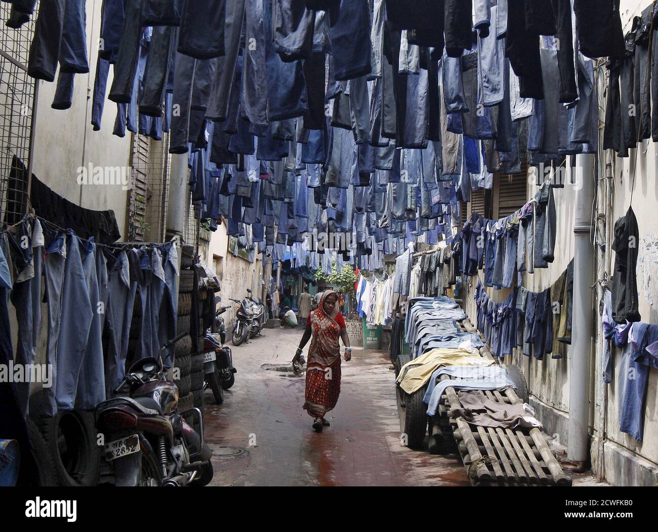 Une femme marche à travers une allée comme les paires de jeans d'occasion  sont accrochées à sécher avant qu'ils soient vendus dans un marché de  vêtements d'occasion à Kolkata, Inde, le 29