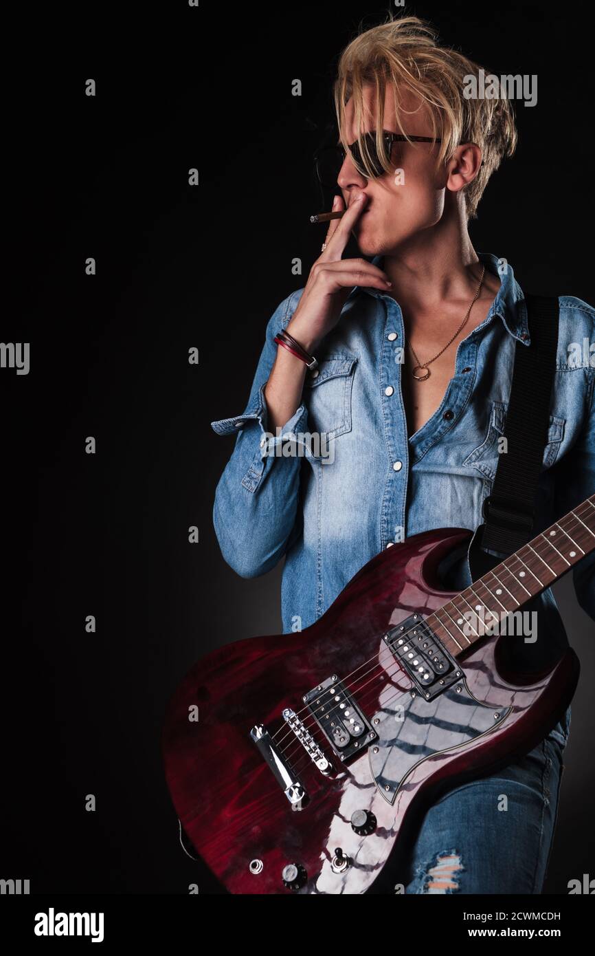 vue latérale d'un jeune guitariste fumant et jouant à son guitare électrique en studio Banque D'Images