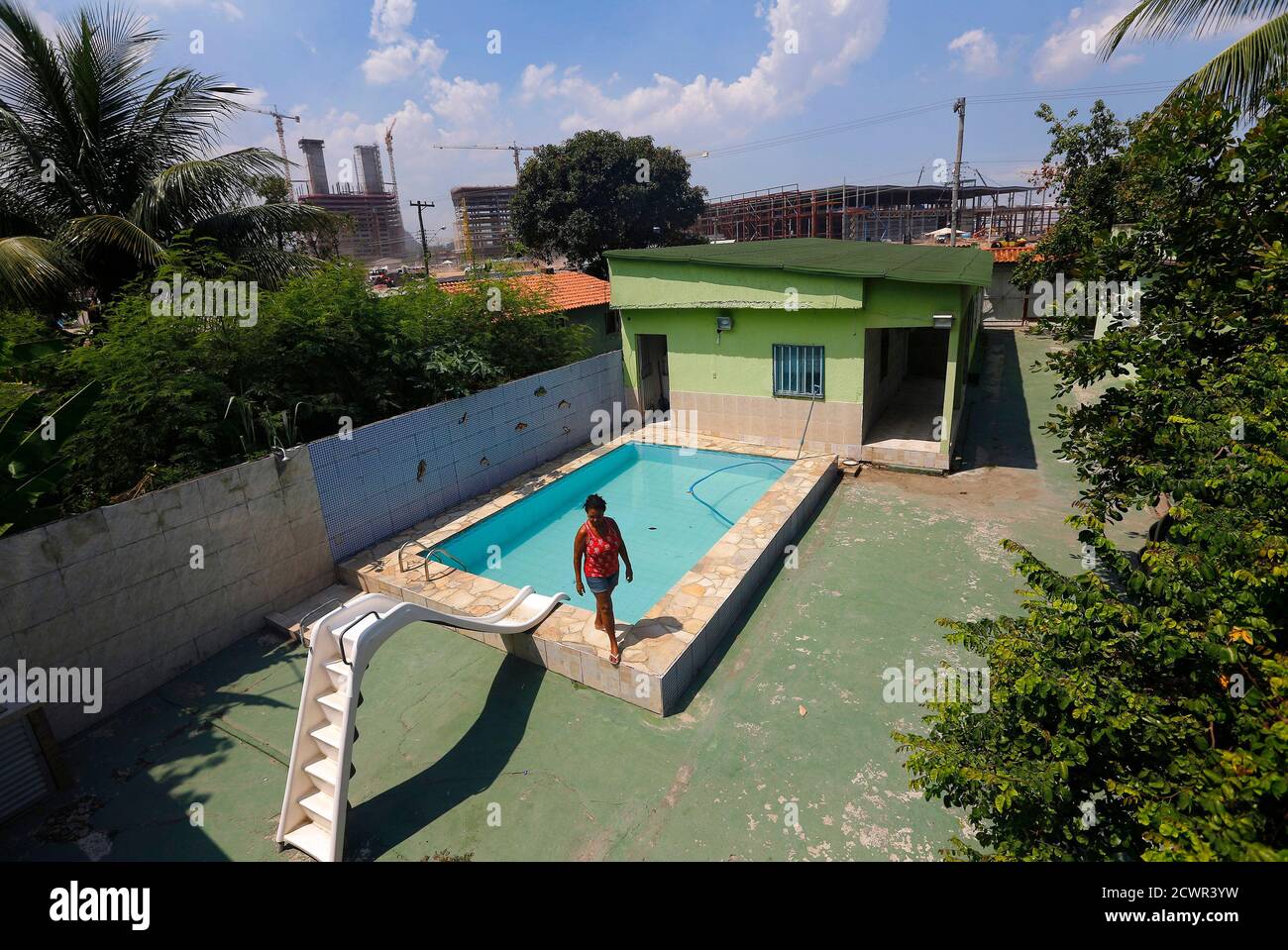 Marcias Lemos 57 Walks By A Pool In Her House With Cranes And Construction Work For The Rio 16 Olympic Park Seen In The Background At The Vila Autodromo Favela In Rio