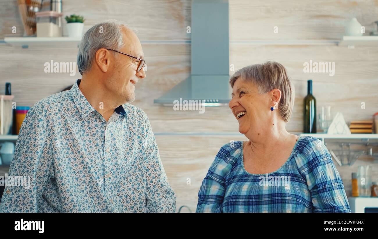 Couple senior riant en regardant l'appareil photo dans la cuisine. Joyeux homme et femme souriant et riant. Heureux personnes âgées retraités dans la maison confortable appréciant la vie Banque D'Images