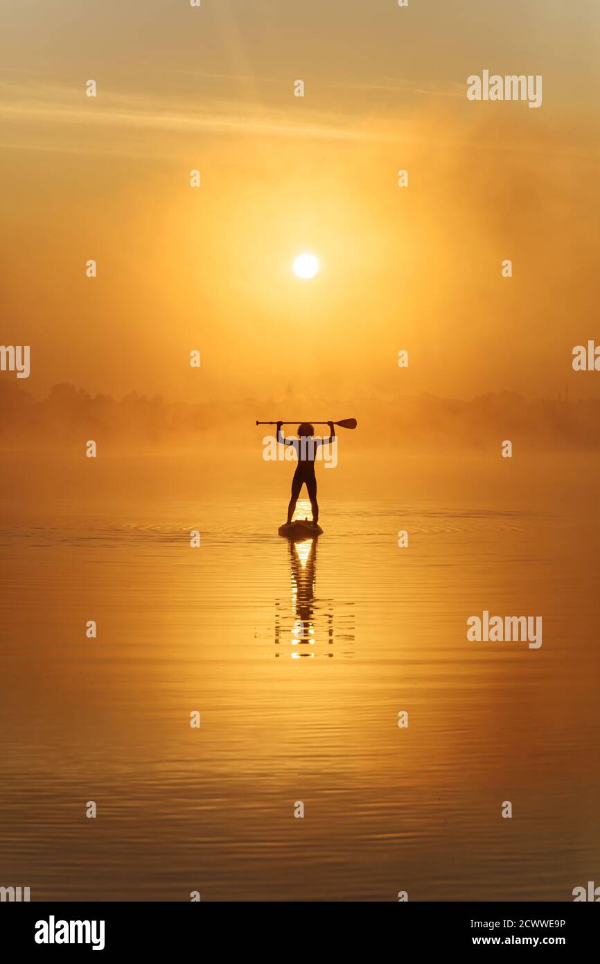 Silhouette d'homme fort pagayant sur le plan supérieur à la mode lac Banque D'Images