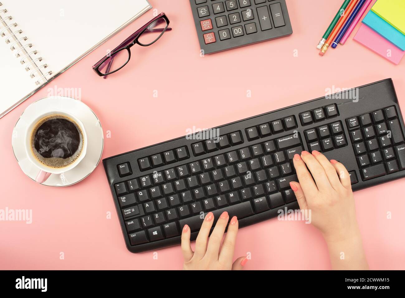 Espace de travail Flat Lay. Femme travaillant sur pc, tasse de café, calculatrice, ordinateur, ordinateur portable, planificateur et stationnaire avec espace de copie sur fond de table rose. Banque D'Images