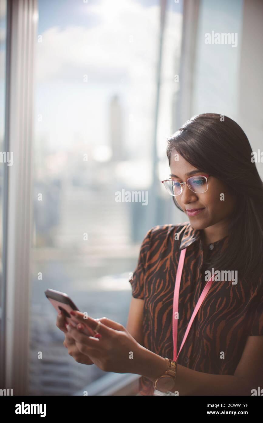 Jeune femme d'affaires utilisant un smartphone à la fenêtre du bureau Banque D'Images