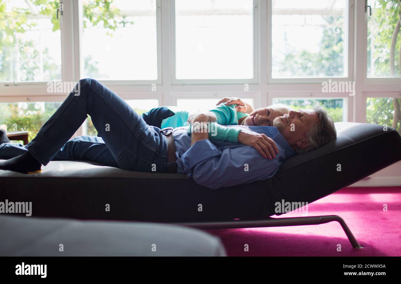 Un couple affectueux se câline sur une chaise longue à la fenêtre ensoleillée Banque D'Images