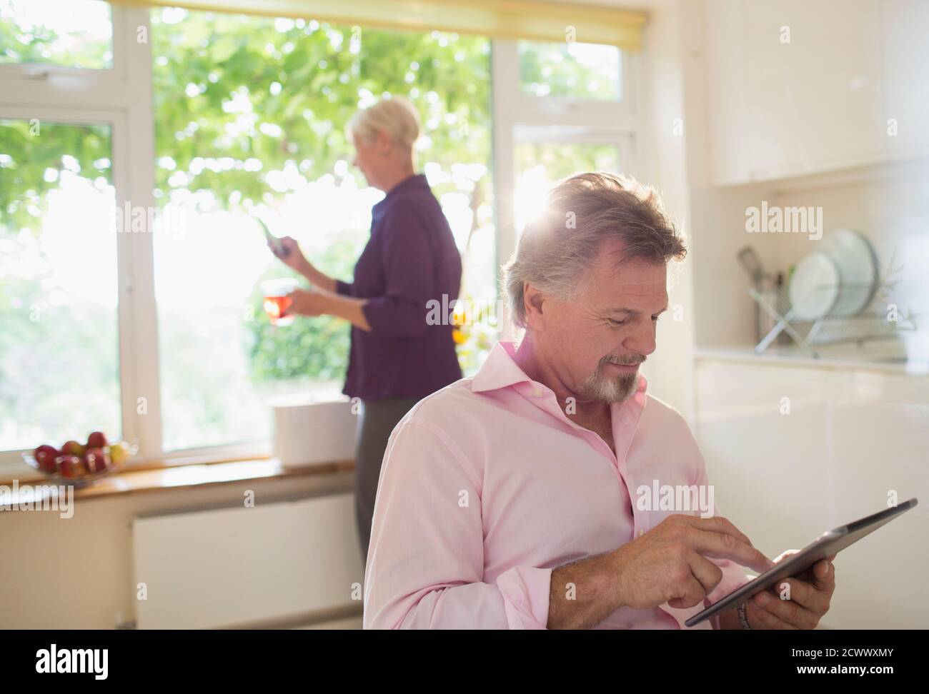 Homme senior utilisant une tablette numérique dans la cuisine ensoleillée du matin Banque D'Images