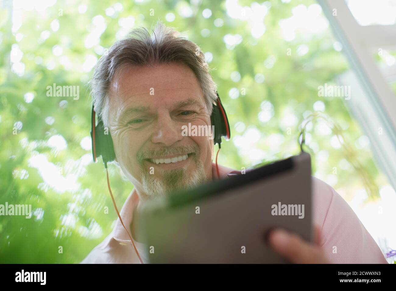 Homme senior souriant écoutant de la musique avec des écouteurs et du numérique tablette Banque D'Images
