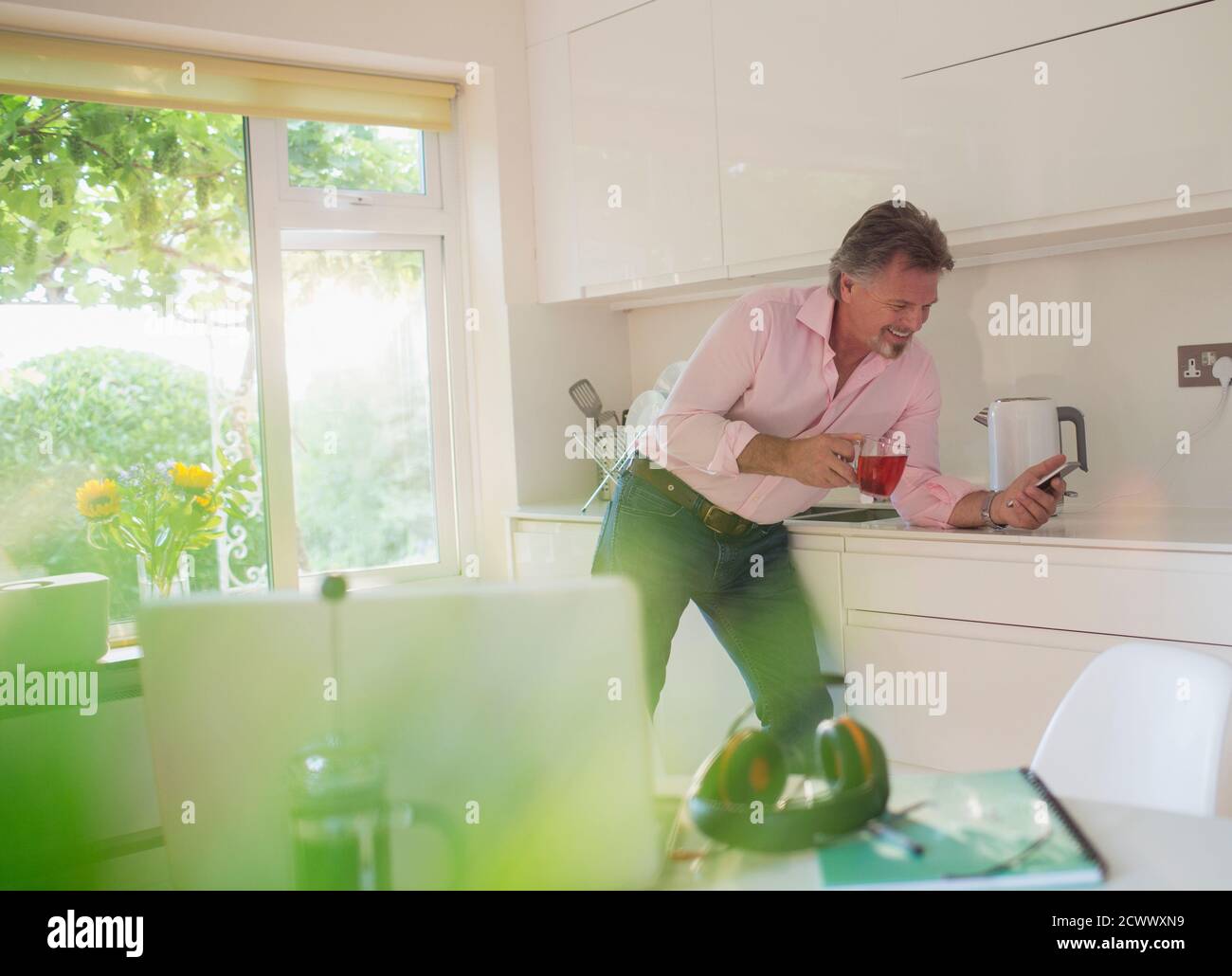 Homme senior qui boit du thé et utilise un smartphone sous le soleil cuisine Banque D'Images