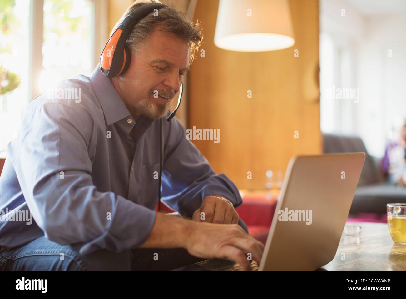 Homme âgé avec casque utilisant un ordinateur portable sur le canapé du salon Banque D'Images