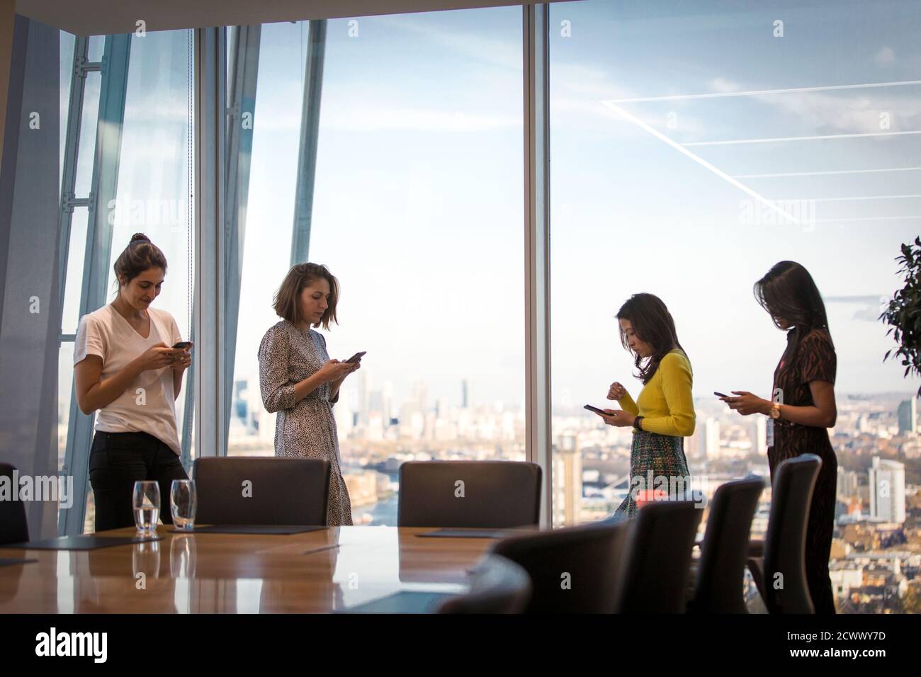 Femmes d'affaires utilisant des téléphones intelligents à la fenêtre de bureau en hauteur Banque D'Images