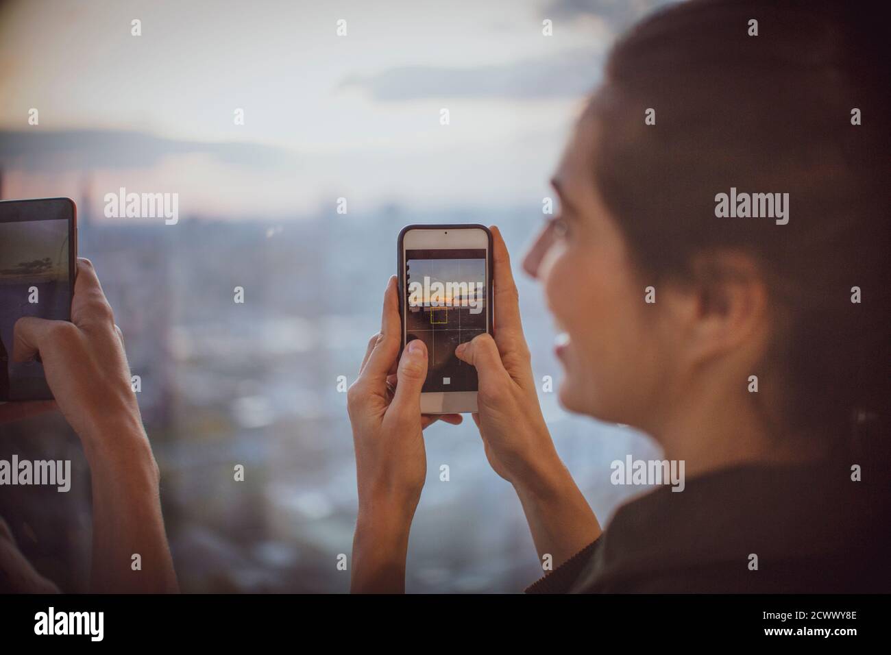 Femme d'affaires avec un téléphone photo qui photographie le coucher du soleil à la fenêtre Banque D'Images