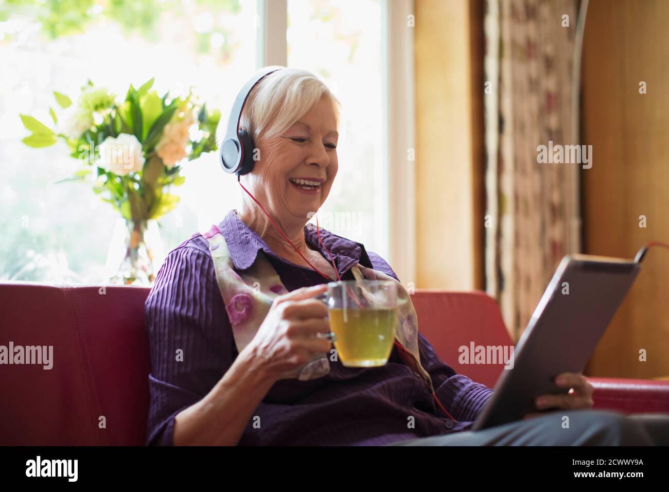 Bonne femme âgée avec un casque et une tablette numérique pour boire du thé Banque D'Images