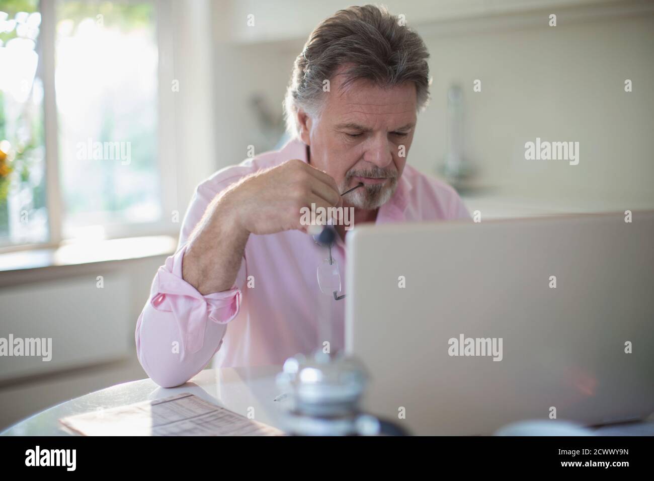 Homme senior travaillant sur un ordinateur portable à la table de cuisine Banque D'Images