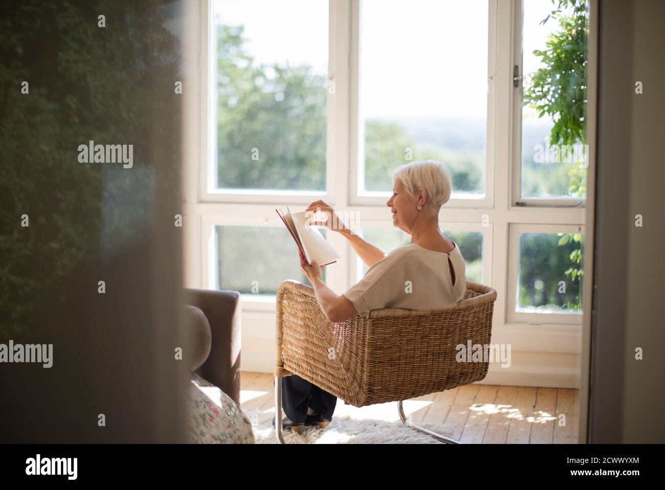 Femme âgée se détendant et lisant un livre dans le fauteuil du salon Banque D'Images