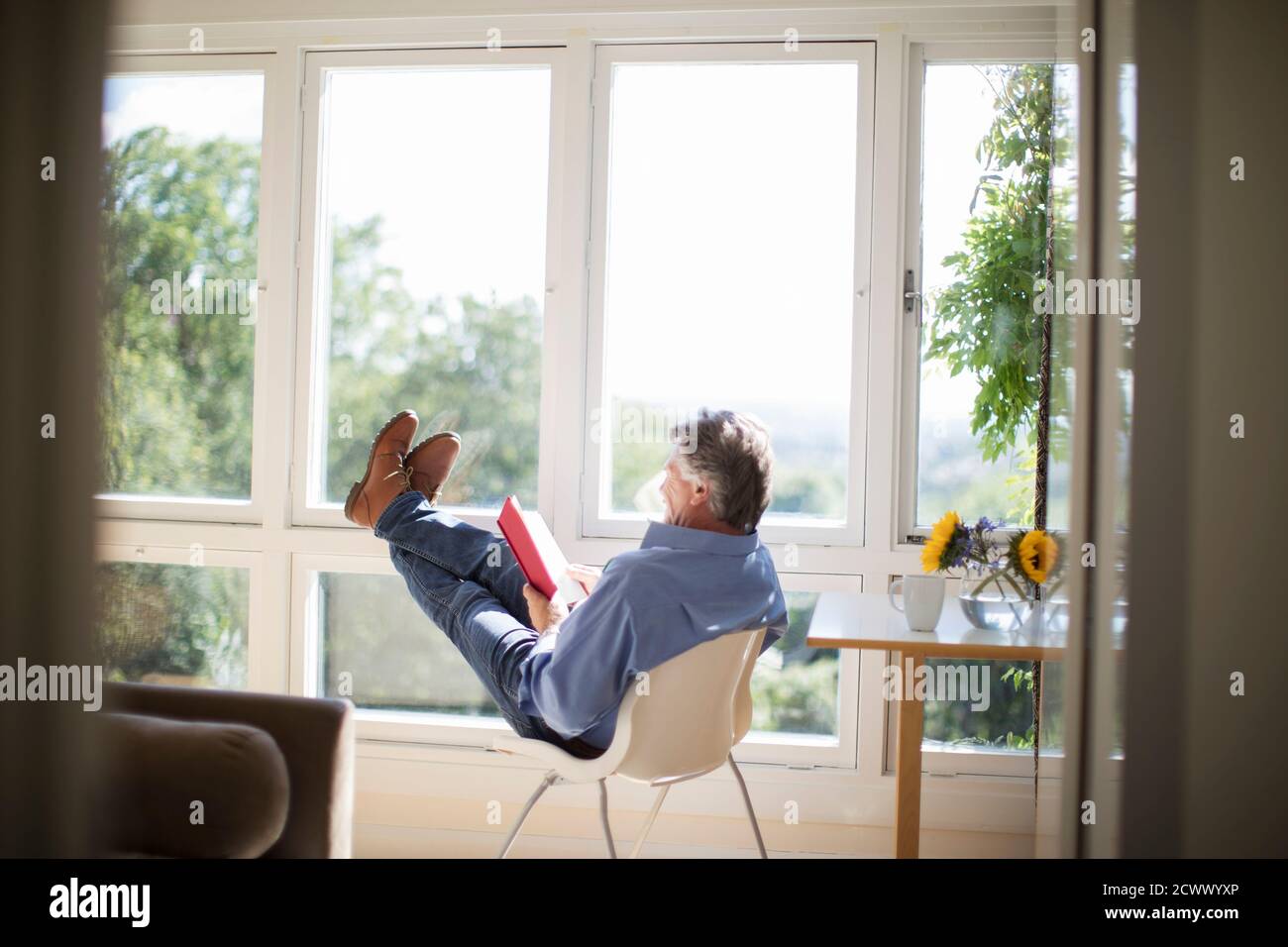 Livre de lecture insouciant, homme âgé, avec ses pieds au soleil fenêtre Banque D'Images