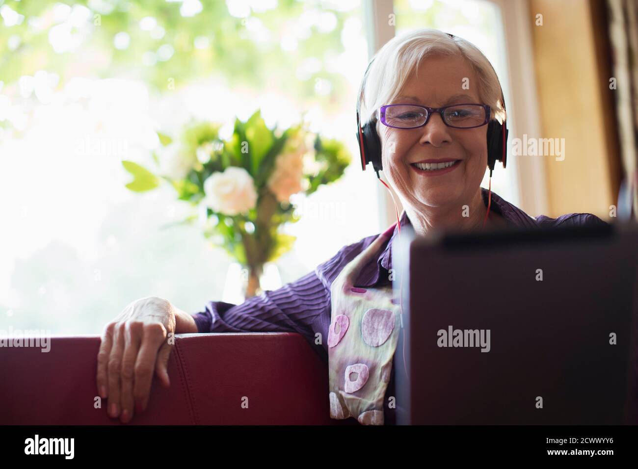 Femme âgée souriante avec un casque utilisant une tablette numérique sur un canapé Banque D'Images
