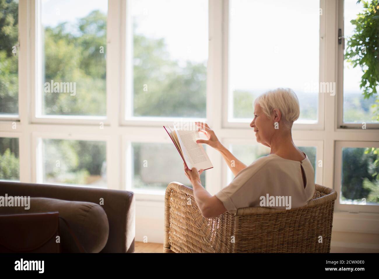Femme sénior se détendant et lisant un livre dans un salon ensoleillé Banque D'Images