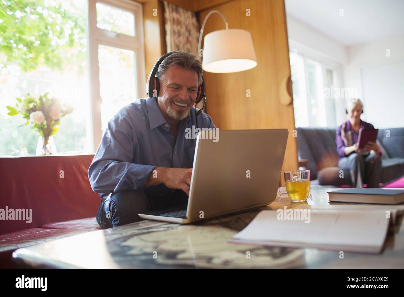Homme senior heureux avec un casque utilisant un ordinateur portable dans le salon Banque D'Images