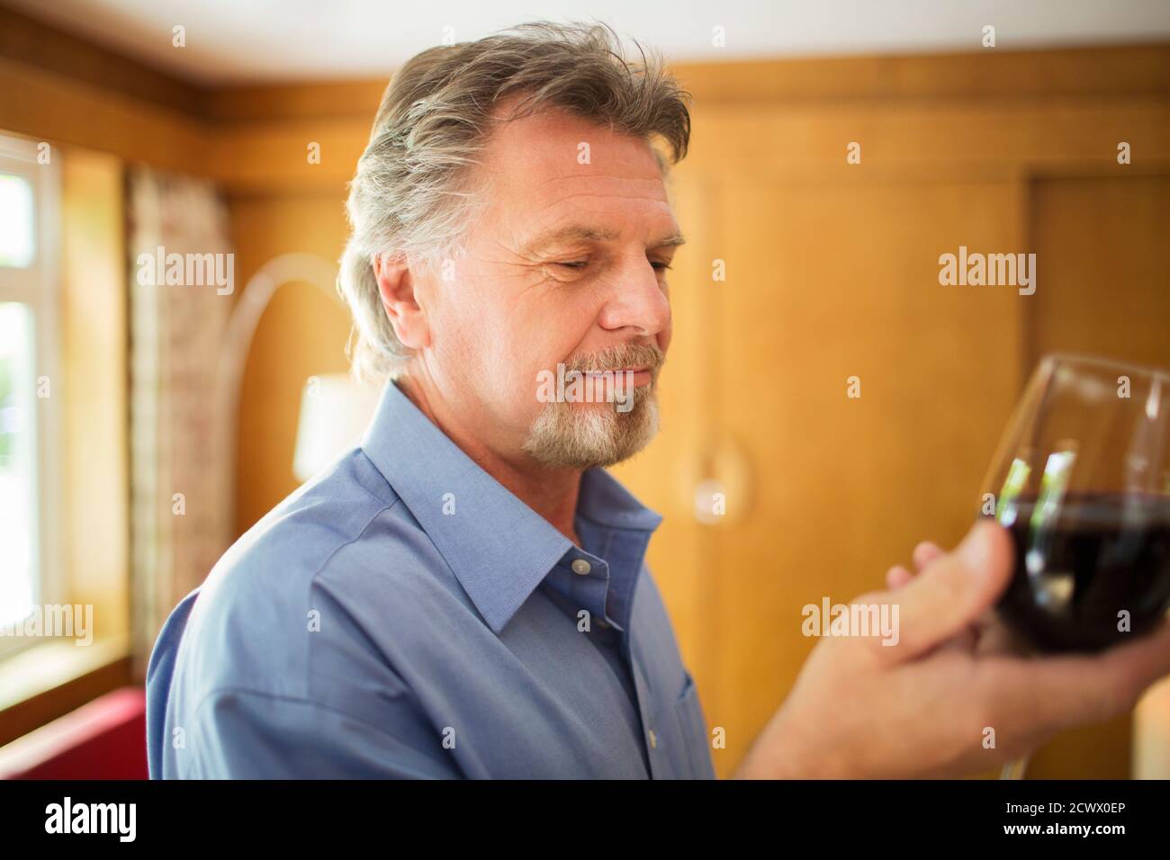 Homme senior qui boit du vin rouge à la maison Banque D'Images