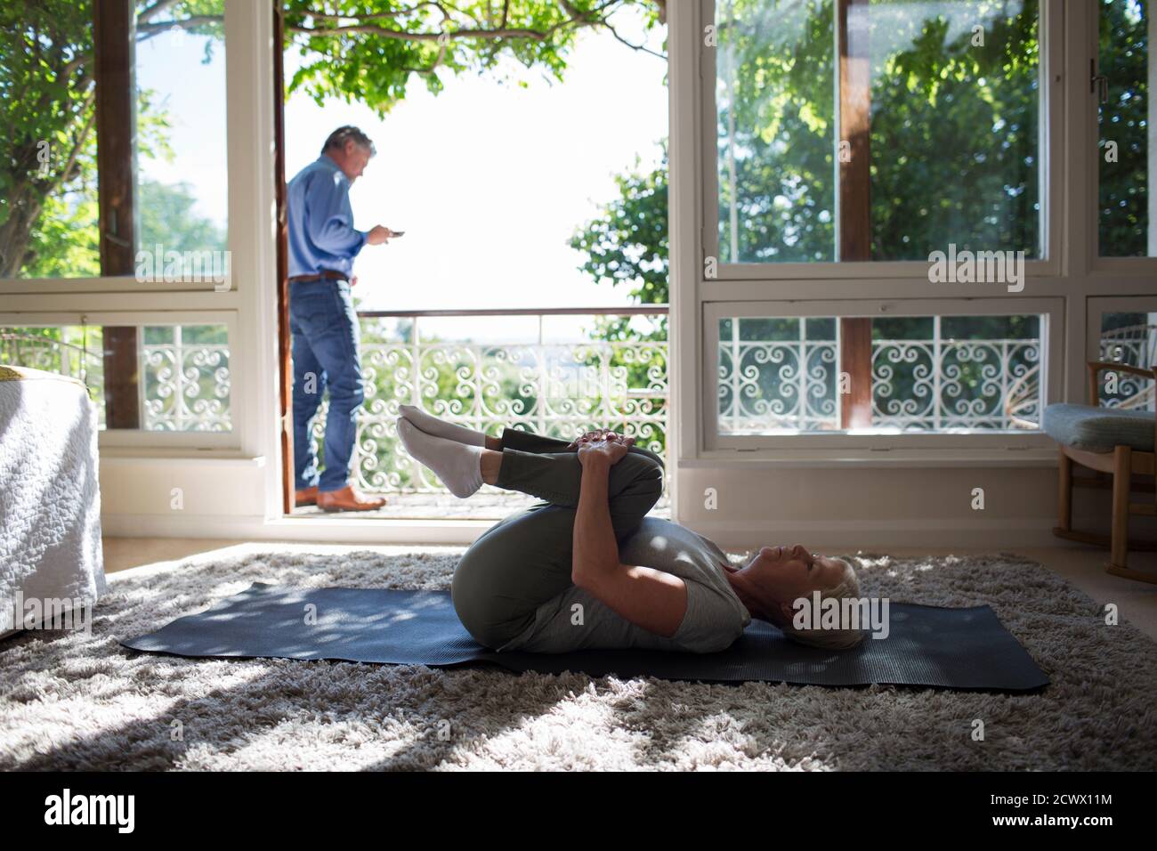 Femme âgée s'étirant sur un tapis de yoga à la porte du balcon d'été Banque D'Images