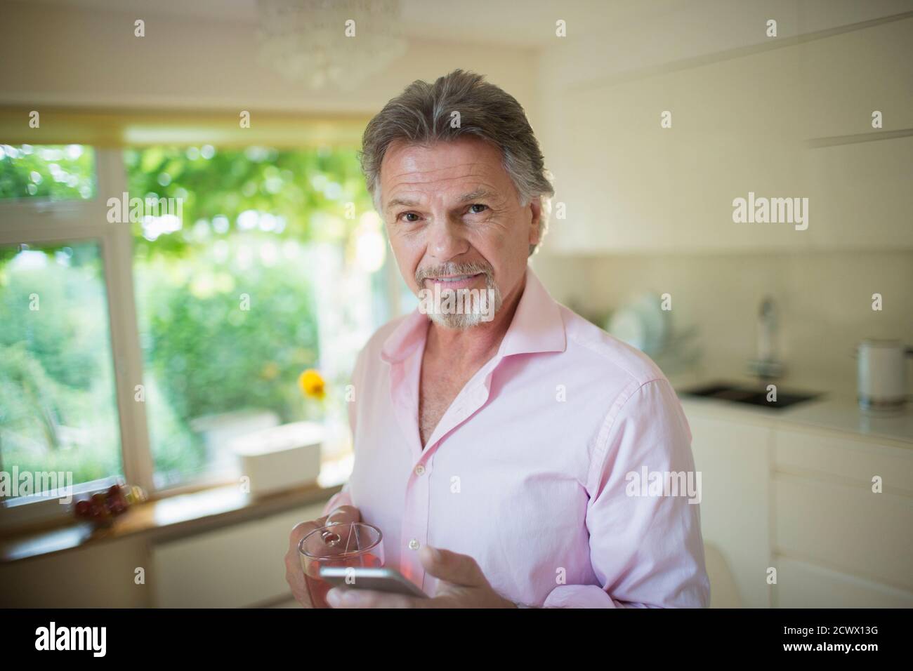 Portrait d'un homme expérimenté confiant avec un smartphone et un thé cuisine Banque D'Images