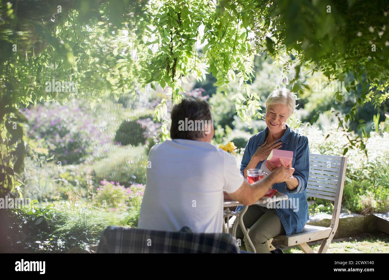 Une femme âgée heureuse ouvre un cadeau de son mari sur le patio d'été Banque D'Images