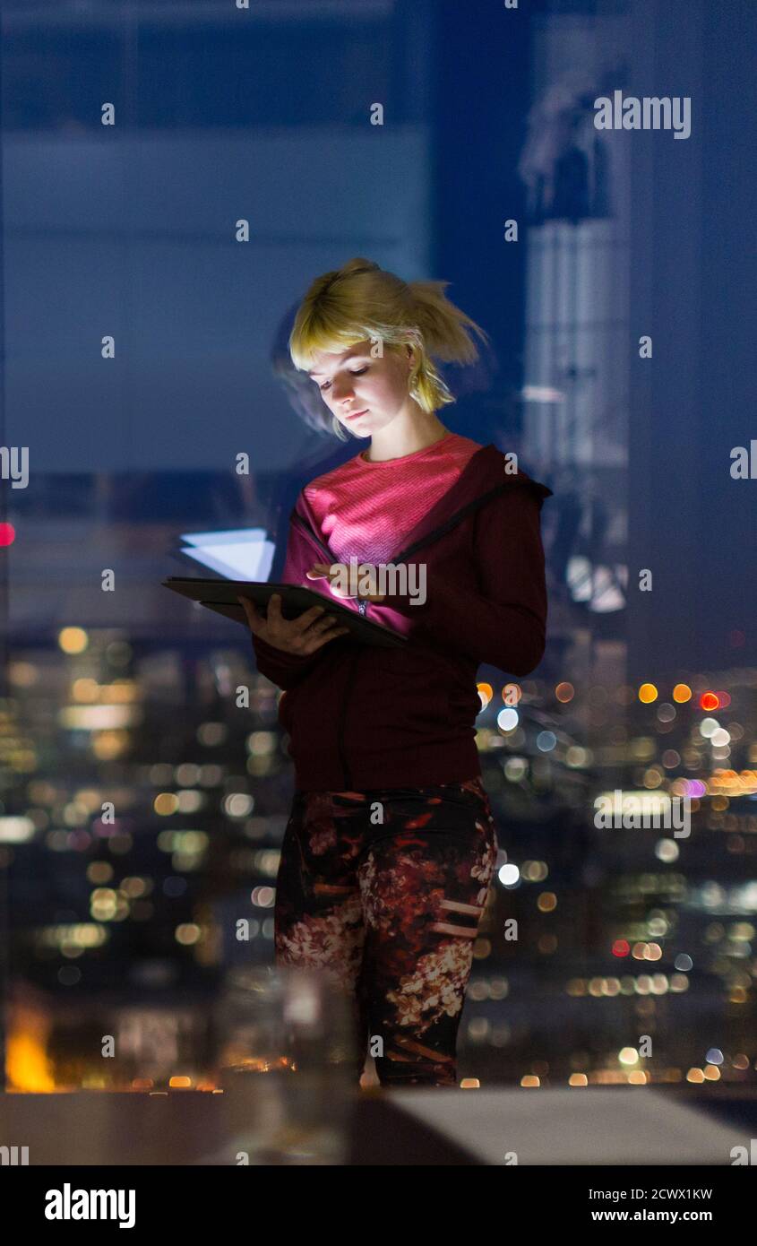 Jeune femme d'affaires avec tablette numérique travaillant tard à la fenêtre du bureau Banque D'Images