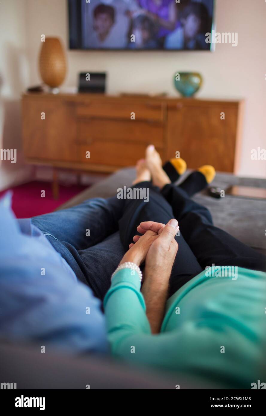 Couple affectueux tenant les mains et regardant la télévision sur un canapé Banque D'Images