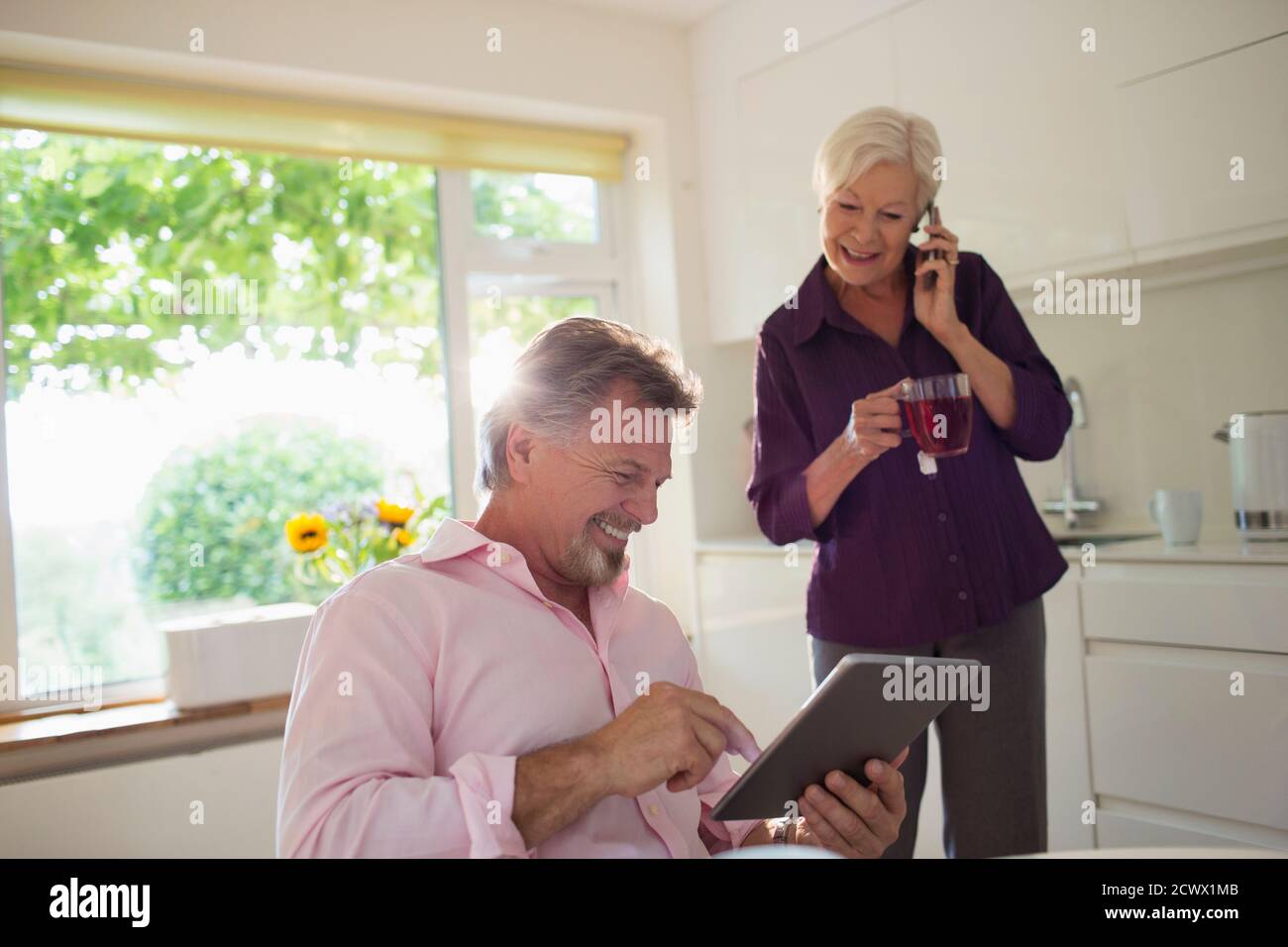 Couple senior heureux utilisant une tablette numérique et un smartphone cuisine Banque D'Images