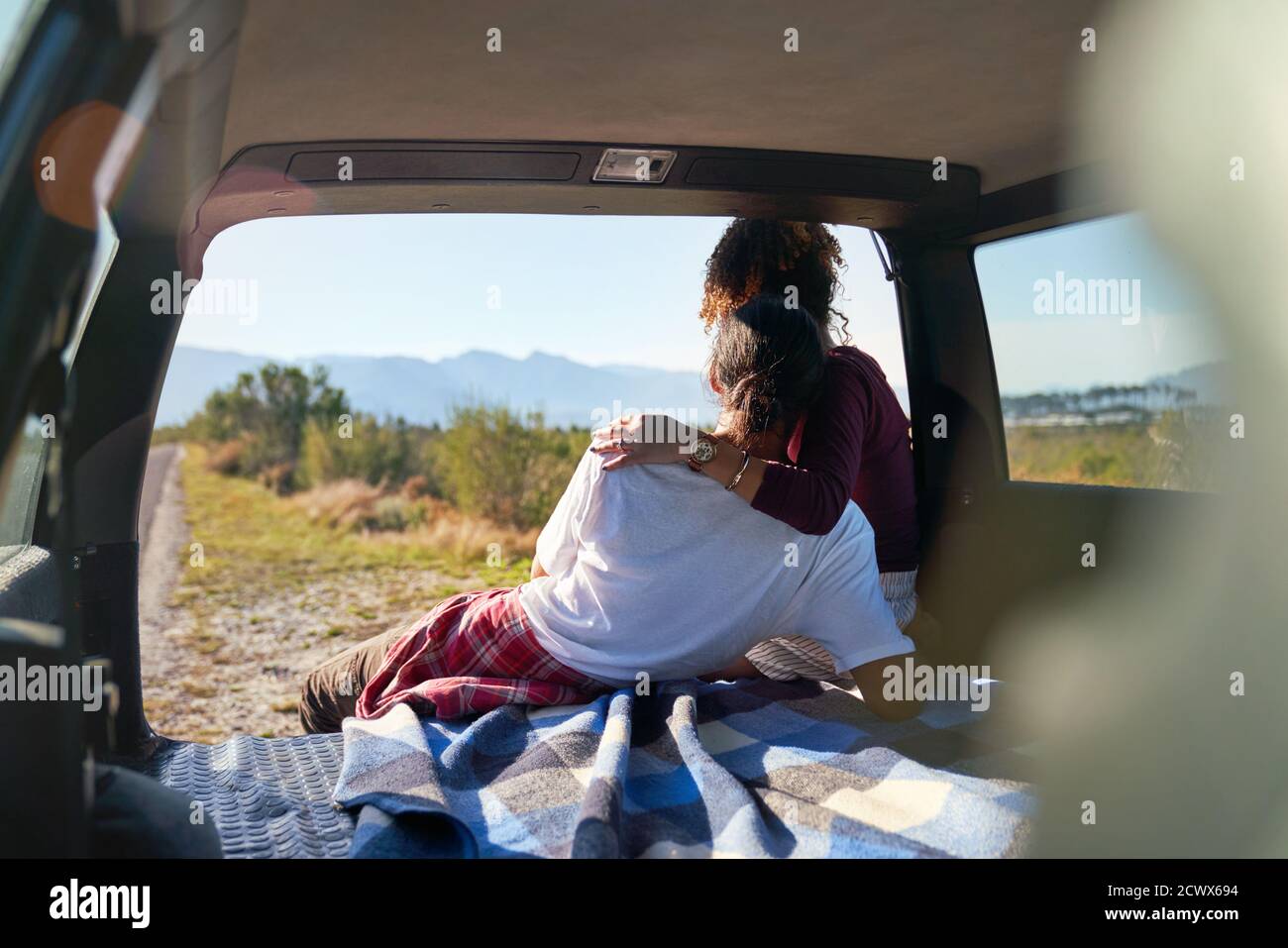 Jeune couple affectueux jouissant d'une vue ensoleillée sur la nature depuis l'arrière voiture Banque D'Images