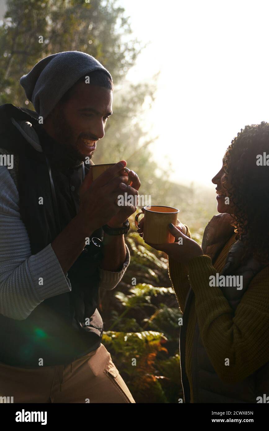 Un jeune couple de randonneurs heureux qui boit du café dans des bois ensoleillés Banque D'Images