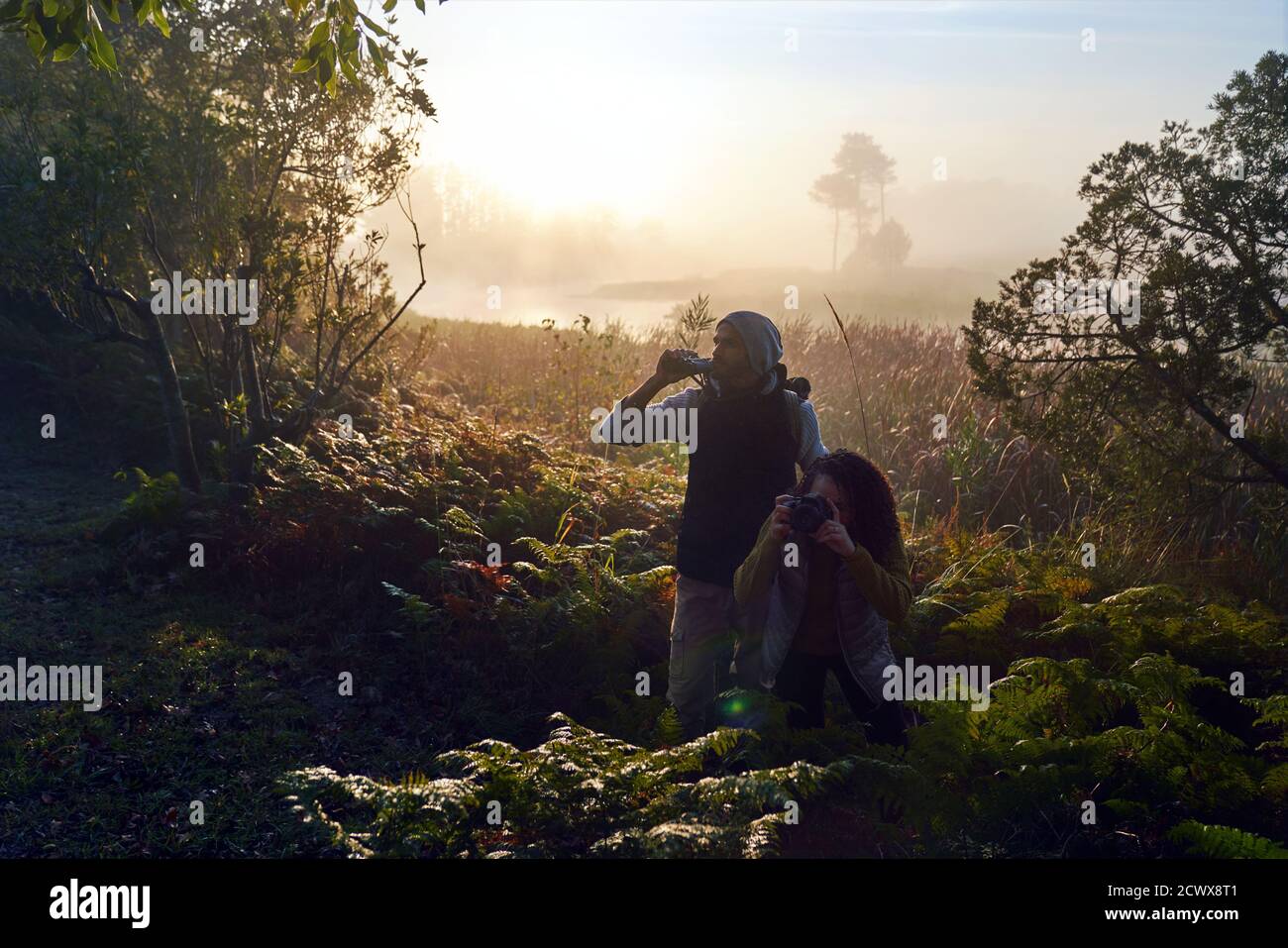 Curieux jeune couple randonnée avec jumelles et appareil photo dans le soleil bois Banque D'Images