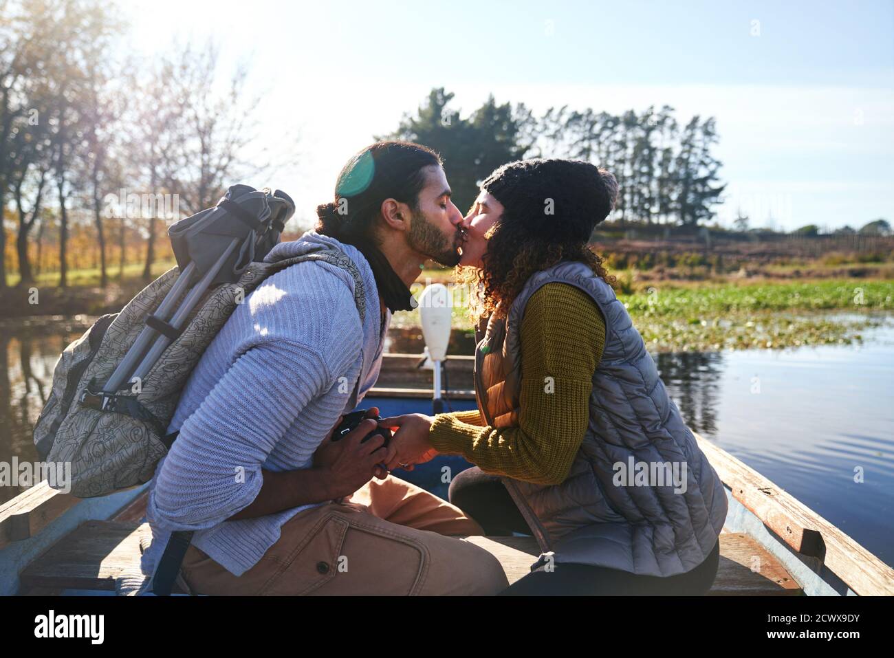 Un jeune couple affectueux s'embrasse en barque sur un lac d'automne ensoleillé Banque D'Images