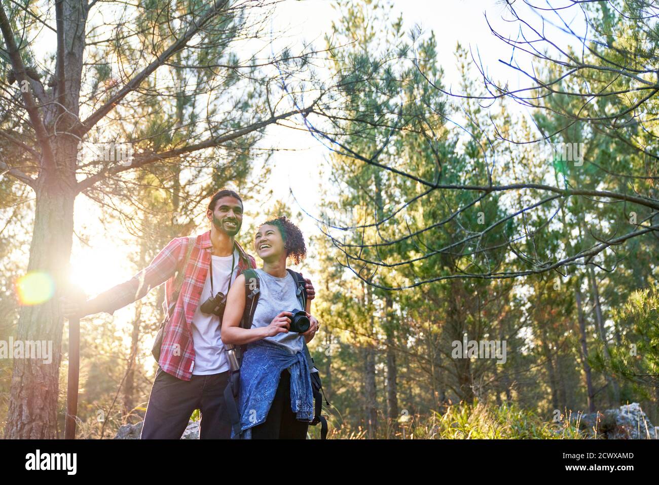 Joyeux jeune couple randonnée avec appareil photo et jumelles dans le soleil bois Banque D'Images