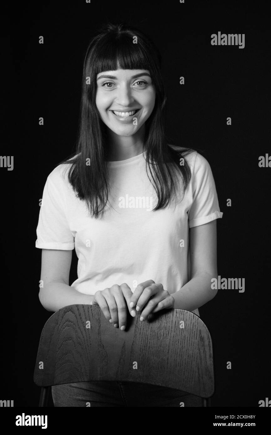 Portrait studio d'une jolie femme brune dans un t-shirt blanc, sur fond noir Uni, souriant, regardant l'appareil photo Banque D'Images