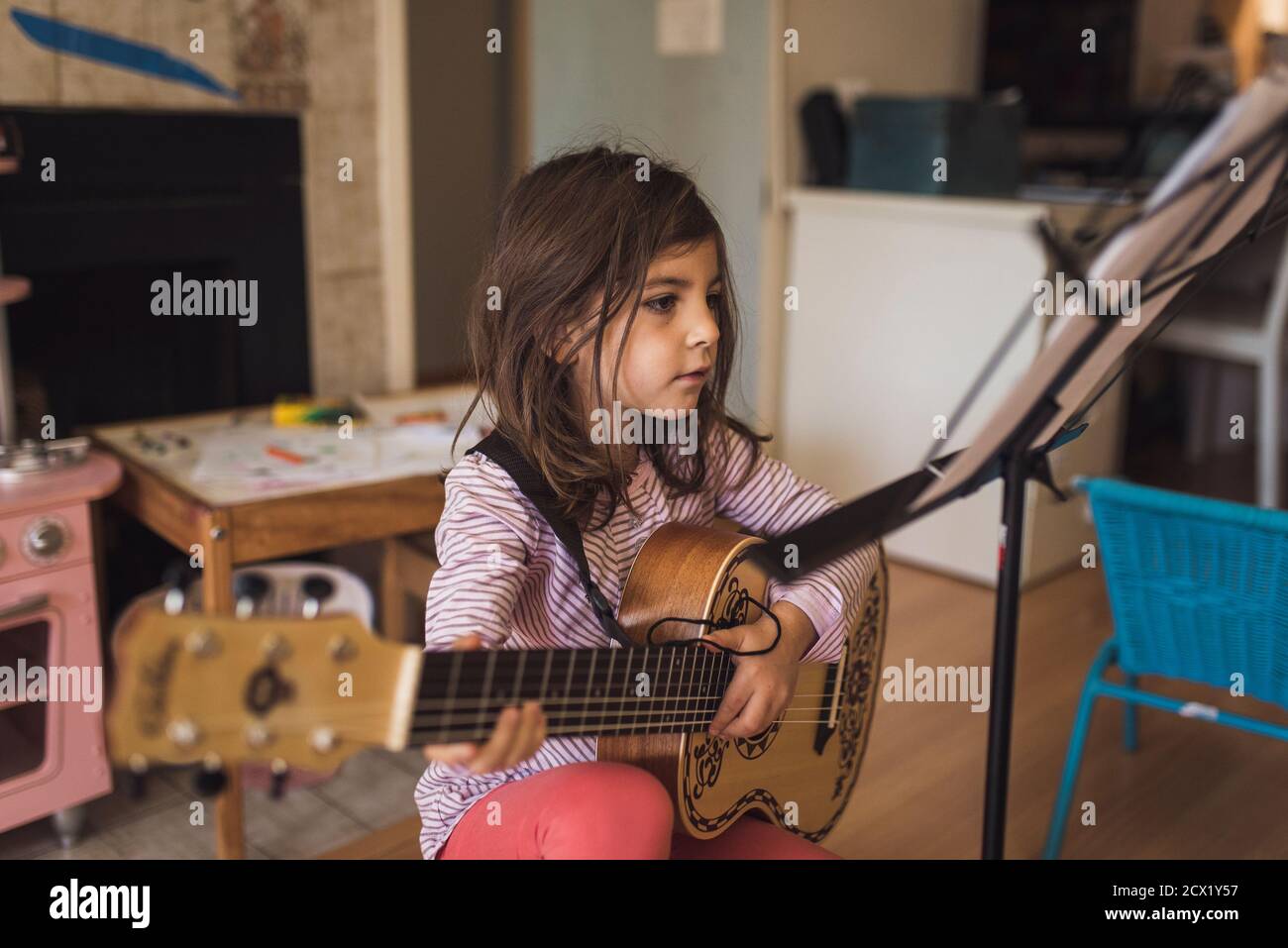 fille de 6 ans avec des cheveux foncés pratiquant la leçon de guitare dans la salle de jeux Banque D'Images