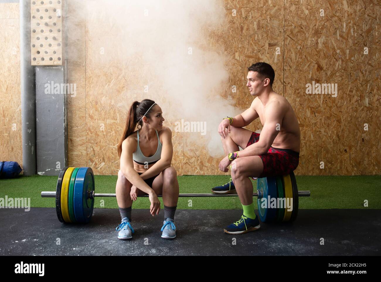 Un homme et une femme sans crier dans les vêtements de sport souriant et  ayant belle conversation en s'asseyant sur le barbell dans la salle de gym  Photo Stock - Alamy